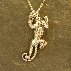 Puede incluir: Un collar de cadena de oro con un colgante de leopardo detallado y manchado.