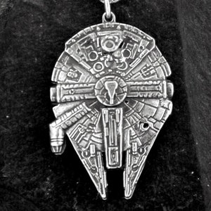 Puede incluir: Un collar de plata con un colgante detallado con forma de la nave espacial Millennium Falcon de Star Wars.