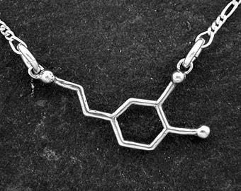 May include: A silver necklace with a pendant shaped like a chemical molecule. The pendant is a simple, geometric design.