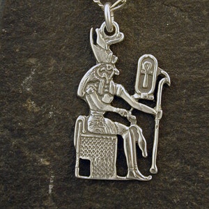 Può includere: Collana con ciondolo in argento raffigurante una divinità egizia seduta su un trono, che tiene uno scettro con un simbolo ankh.