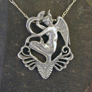 May include: A silver necklace with a pendant featuring a detailed, stylized figure of a woman with wings and a snake. The pendant is attached to a delicate silver chain.