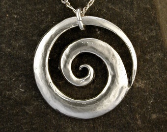 May include: A silver necklace with a spiral pendant. The pendant is a circle with a spiral design in the center. The necklace is on a dark gray background.