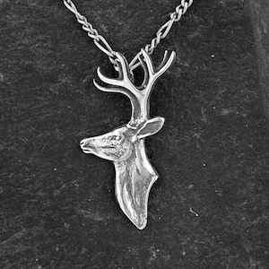 Könnte beinhalten: Eine silberne Halskette mit einem detaillierten Hirschkopf-Anhänger. Die Kette ist eine silberne Gliederkette.