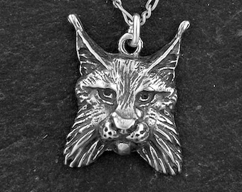 May include: A silver pendant necklace featuring a detailed, realistic sculpture of a lynx's head. The lynx has a fierce expression with large, pointed ears and a bushy beard.