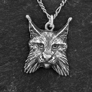May include: A silver pendant necklace featuring a detailed, realistic sculpture of a lynx's head. The lynx has a fierce expression with large, pointed ears and a bushy beard.