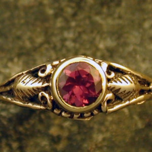 May include: A gold ring with a red gemstone set in a bezel setting. The ring has a delicate floral design on the band.