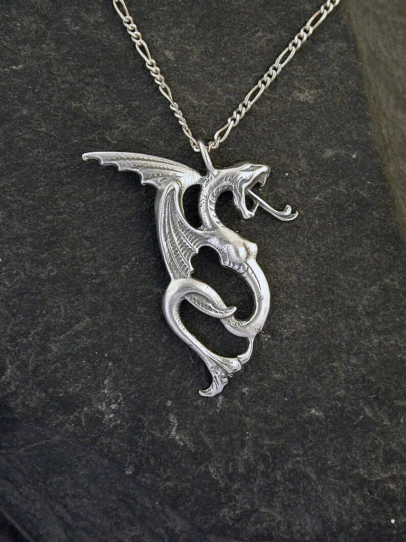 May include: A silver dragon pendant necklace with a detailed design. The dragon is curled up with its wings spread out. The necklace is on a silver chain.