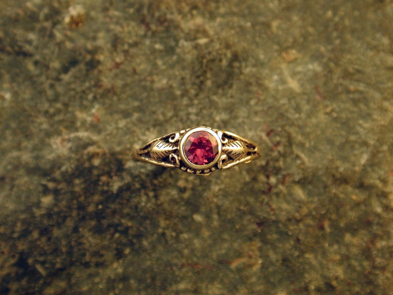 May include: A gold ring with a red gemstone set in a delicate floral design.