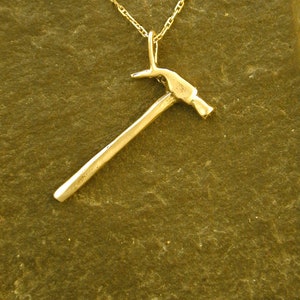 Op de afbeelding: Een gouden hamer hanger ketting. De hamer is een eenvoudig ontwerp met een ronde kop en een lange steel.