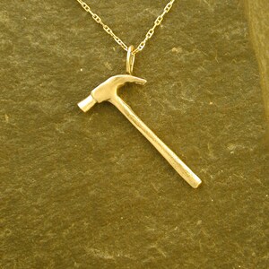 Op de afbeelding: Een gouden hamer hanger ketting. De hamer is een eenvoudig ontwerp met een ronde kop en een rechte steel.