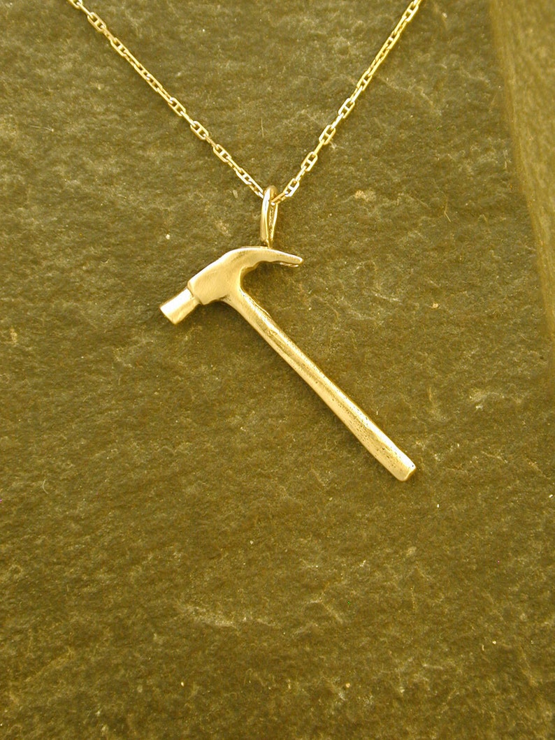 Op de afbeelding: Een gouden hamer hanger ketting. De hamer is een eenvoudig ontwerp met een ronde kop en een rechte steel.
