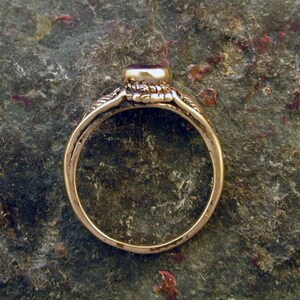 May include: A gold ring with a red gemstone set in a bezel setting. The ring has a simple band and a detailed design around the gemstone.