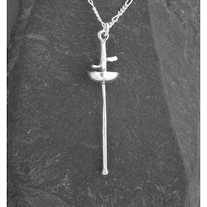 May include: A silver-colored pendant necklace featuring a fencing épée design. The pendant has a detailed, miniature replica of a fencing sword, including the guard, blade, and handle. The necklace hangs on a delicate silver chain, creating a simple yet elegant accessory.