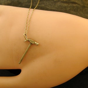Op de afbeelding: Een gouden ketting met een klein hamer hanger.