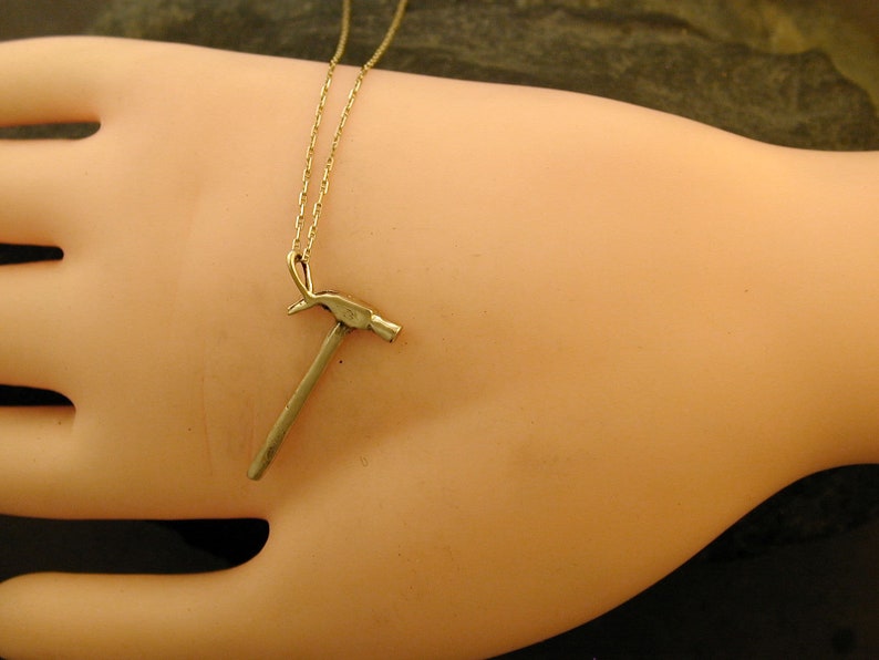 Op de afbeelding: Een gouden ketting met een klein hamer hanger.