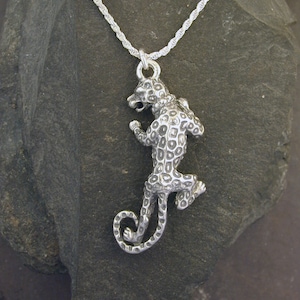 Puede incluir: Un collar de plata con un colgante tridimensional detallado de un leopardo. El colgante está texturizado para parecerse a las manchas del animal.