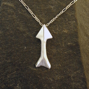 May include: A silver necklace with a simple arrow pendant. The arrow is made of smooth, polished metal and has a pointed tip.