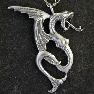 May include: A silver dragon pendant necklace with intricate details. The dragon is curled up with its wings spread out. The necklace is made of a silver chain.