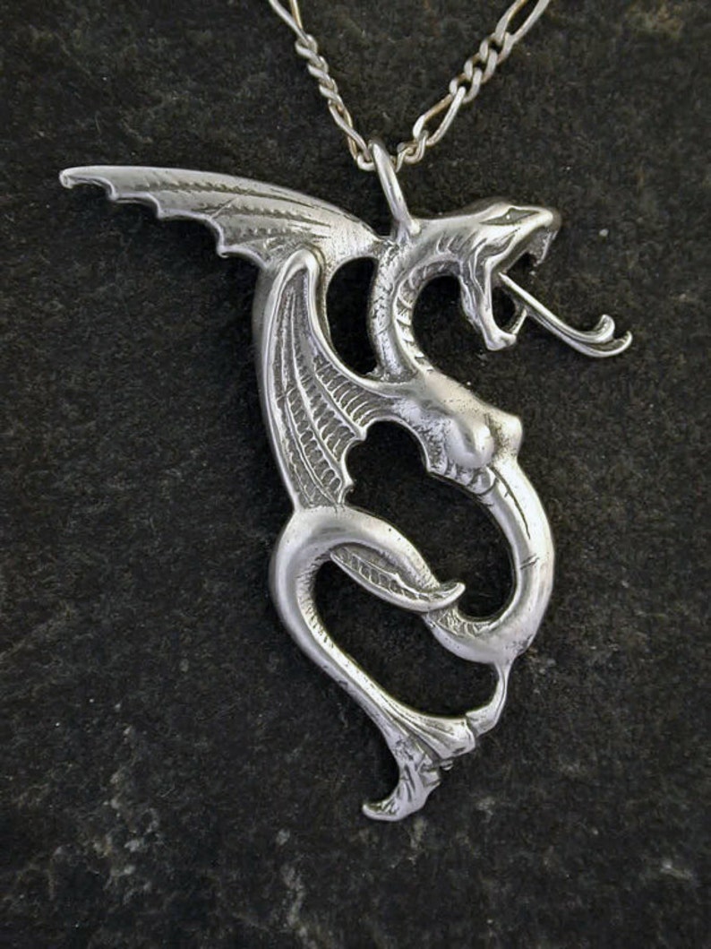May include: A silver dragon pendant necklace with intricate details. The dragon is curled up with its wings spread out. The necklace is made of a silver chain.