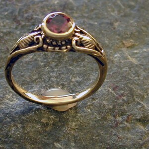 May include: A gold ring with a purple gemstone set in a decorative setting. The ring has a delicate, intricate design.