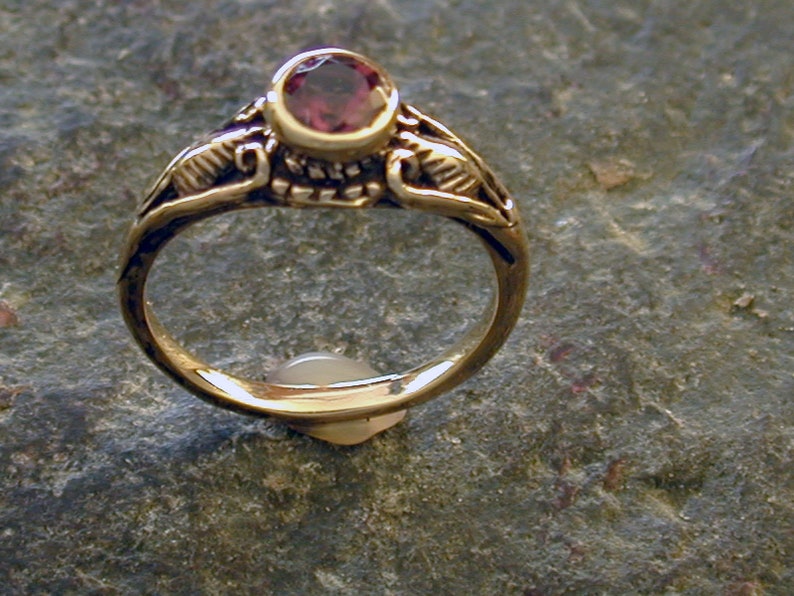 May include: A gold ring with a purple gemstone set in a decorative setting. The ring has a delicate, intricate design.