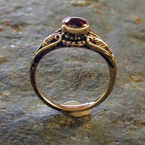 May include: A gold ring with a delicate design featuring a single, round, dark red gemstone.