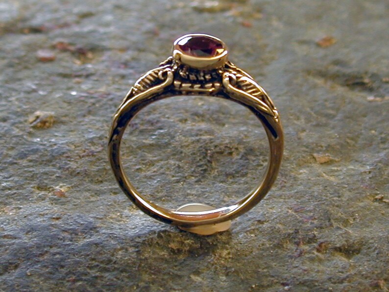 May include: A gold ring with a delicate design featuring a single, round, dark red gemstone.