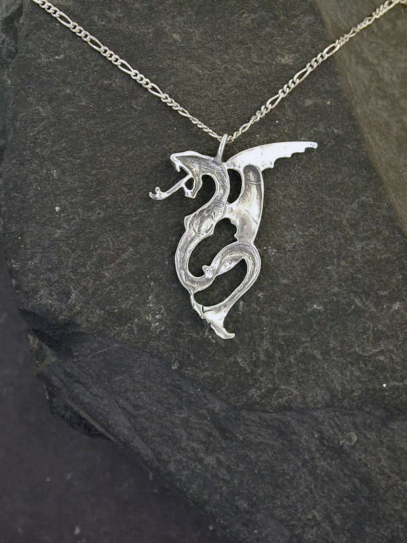 May include: A silver dragon pendant necklace with a detailed design. The dragon is curled up with its wings spread out. The necklace is on a silver chain.
