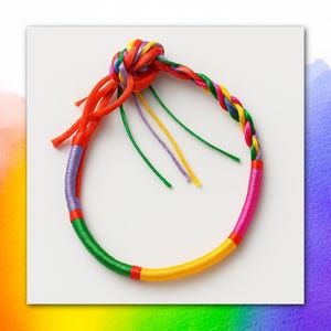 Puede incluir: Una pulsera circular hecha de hilo multicolor envuelto alrededor de un núcleo. El diseño presenta secciones de hilo verde, amarillo, rosa, naranja y morado, con un segmento trenzado y un nudo prominente en la parte superior con extremos sueltos.