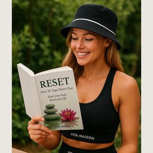 Könnte beinhalten: Eine Frau mit einem schwarzen Fischerhut und einem schwarzen Sport-BH hält ein Buch mit dem Titel "RESET". Das Buchcover zeigt einen Steinhaufen und eine rosa Lotusblume. Der Text auf dem Buch lautet "Dein 30-Tage-Detox-Plan" und "Reset your body. Reset your life."