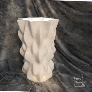 May include: A white, textured vase with a unique, twisted design. The vase has a wide, star-shaped opening and a textured surface. The vase is approximately 12 inches tall and is made of a solid material. The Terra Forma logo is in the bottom right corner.