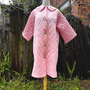May include: A white ceramic mug with a black handle and the text "But First, Coffee" in a bold, black font. The mug is set against a blurred background, suggesting a cozy setting.