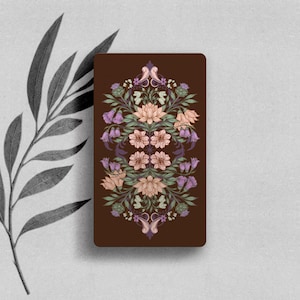 May include: A rectangular card with a dark brown background featuring a symmetrical, intricate botanical illustration. The design includes light pink lotus flowers, purple bell-shaped blossoms, green leaves, and thistle-like elements.
