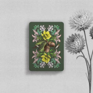May include: A rectangular card with a dark green background featuring a symmetrical botanical illustration of yellow flowers, pink lily-like blossoms, green leaves, and brown acorns. The design is centered on the card, which is displayed vertically.