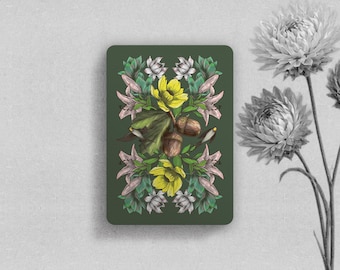 May include: A rectangular card with a dark green background featuring a symmetrical botanical illustration of yellow flowers, pink lily-like blossoms, green leaves, and brown acorns. The design is centered on the card, which is displayed vertically.