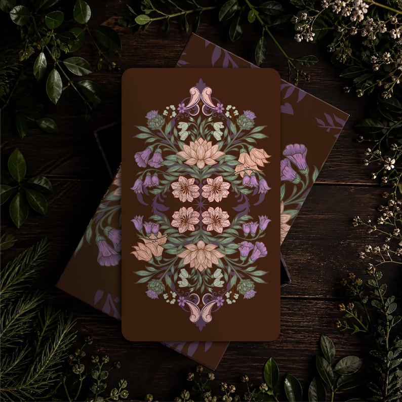 May include: A rectangular card with a dark brown background featuring a symmetrical, intricate botanical illustration. The design includes light pink lotus-like flowers, purple bell-shaped blossoms, and green foliage arranged in a vertical pattern.