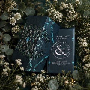 May include: A dark blue tarot deck box featuring a floral and celestial illustration with a star and crescent moon. The box displays the text MERAKI TAROT 4TH EDITION, BOUCHETTE & CO, OBJECTS OF ENCHANTMENT, and 2026 BOUCHETTE & CO, LLC.