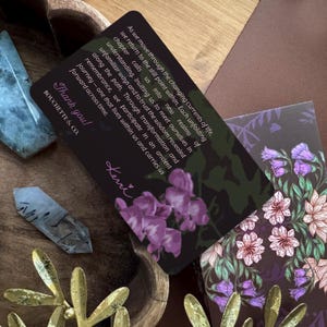 May include: A rectangular black card featuring purple flower illustrations and white text that reads: As we move through the changing currents of life, we return to the still point within. Each unfolding chapter calls us into new realms of understanding, inviting us to meet ourselves in unfamiliar ways and to trust the wisdom revealed along the path. Through transformation and remembrance, we participate in an ancient journey&mdash;one that lives within us and carries us forward across time. Thank you! BOUCHETTE & CO. Kerri.