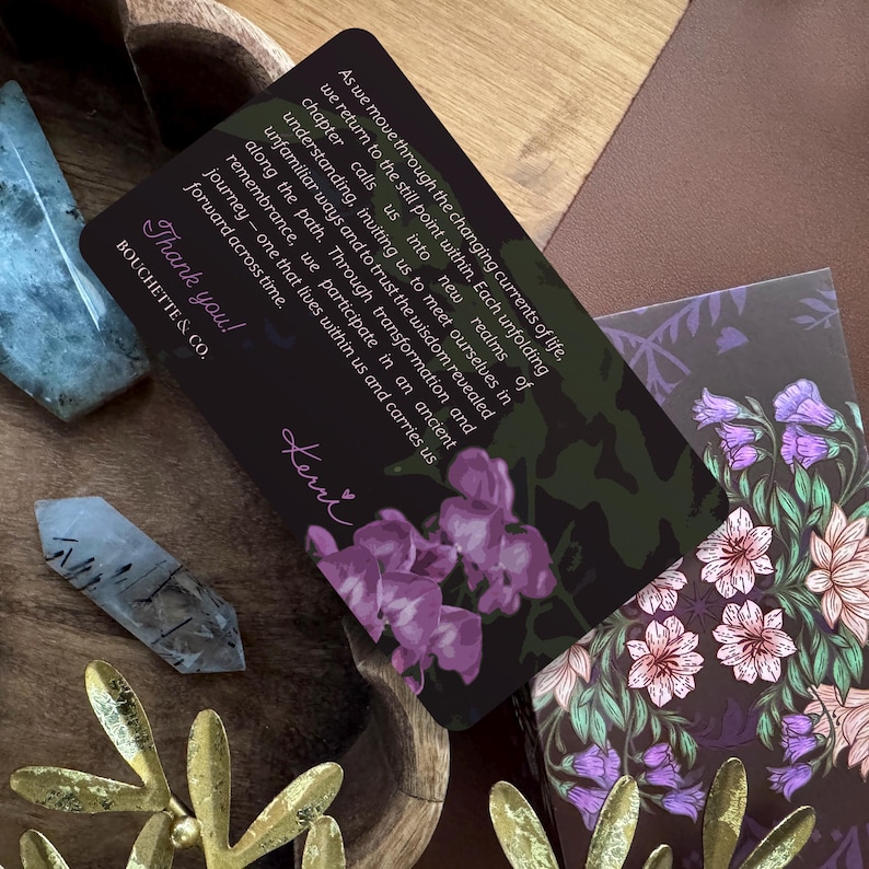 May include: A rectangular black card featuring purple flower illustrations and white text that reads: As we move through the changing currents of life, we return to the still point within. Each unfolding chapter calls us into new realms of understanding, inviting us to meet ourselves in unfamiliar ways and to trust the wisdom revealed along the path. Through transformation and remembrance, we participate in an ancient journey&mdash;one that lives within us and carries us forward across time. Thank you! BOUCHETTE & CO. Kerri.