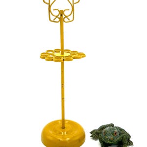 May include: A vintage yellow metal umbrella stand with a decorative top and a circular base. Next to it is a green frog figurine with red eyes. The stand is approximately 24 inches tall.