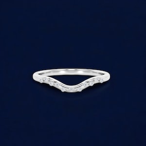 Peut inclure: Une bague argentée incurvée, ornée de petites pierres précieuses transparentes. Le design en forme de vague est mis en valeur par les pierres espacées régulièrement. L'anneau est présenté sur un fond bleu foncé, soulignant son élégance.