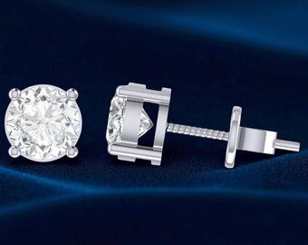 May include: A pair of diamond stud earrings. Each earring has a round, brilliant-cut diamond set in a silver or white gold prong setting. The earrings are shown against a dark blue background, emphasising their sparkle.