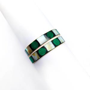 May include: Two matching bracelets with a geometric design. The bracelets feature alternating squares of white and black, with green circular accents. The bracelets are made of a gold-colored metal.
