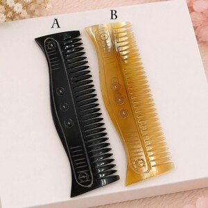Puede incluir: Dos peines para el cabello etiquetados como A y B. El peine A es de color negro sólido y el peine B es de color ámbar translúcido. Ambos peines cuentan con un mango largo y curvo con una serie de hendiduras circulares y dientes finos.
