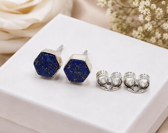 May include: A pair of hexagonal stud earrings featuring deep blue lapis lazuli stones with gold-colored flecks, set in silver-toned metal frames. The set includes two matching silver-toned metal earring backs for secure fastening.
