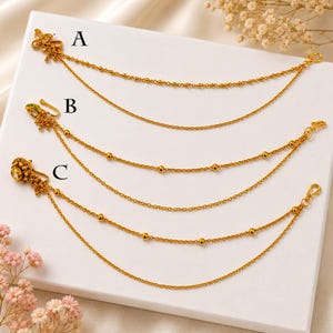 May include: Three gold-toned nose chains labelled A, B, and C. Each chain features a decorative element on one end, including a butterfly, a green-accented piece, and a circular floral design, with small beads along the delicate gold chains.