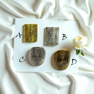 May include: Four metal rings with unique designs are displayed on a white surface. Two rings have a square spiral design, and two have a rounded spiral design. The rings are in gold and silver tones.