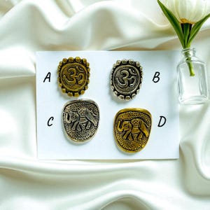 May include: Four antique-style rings with different designs. Two rings feature the Om symbol, and the other two showcase an elephant. The rings are in gold and silver tones, with a textured finish. The rings are displayed on a white surface.