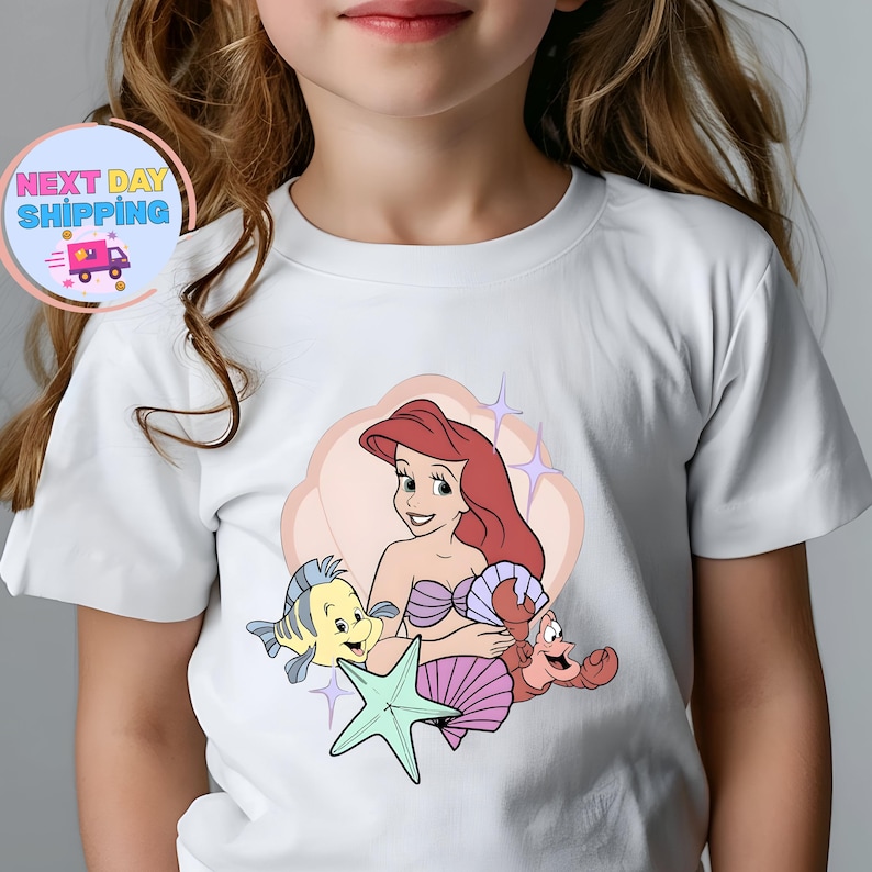 Puede incluir: Camiseta blanca con una ilustraci&oacute;n de dibujos animados de Ariel de La Sirenita, con Flounder, Sebasti&aacute;n y una estrella de mar. La imagen incluye el texto "Next Day Shipping" en un dise&ntilde;o circular con un cami&oacute;n de reparto.