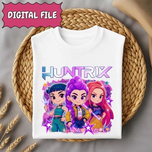 May include: White t-shirt featuring the word "HUNTRIX" in blue and purple, with three cartoon characters in the center. The characters have different hair colors and outfits, surrounded by stars and a purple background. The top left corner has the text "DIGITAL FILE".